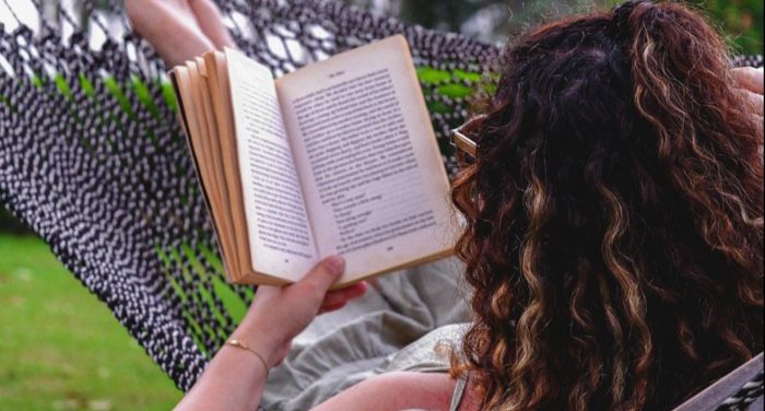 fair skinned person with long curly hair reading in a hammock outside.jpg.optimal