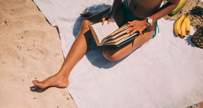 tan skinned woman sitting on the beach and reading a book.jpg.optimal