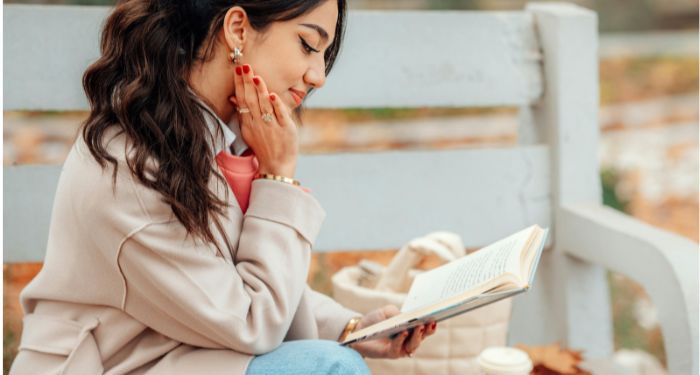 a light tanned skin woman sitting on a bench and reading a book.jpg.optimal