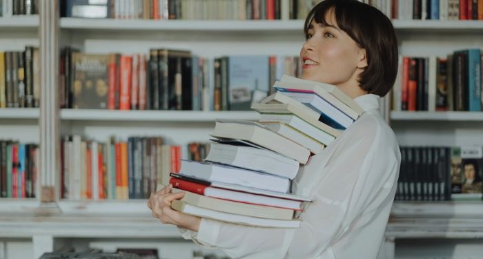 fair skinned Asian woman smiling and holding a huge stack of books.jpg.optimal